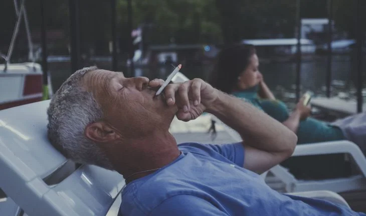 a retired man on a sun lounger smoking a cigarette